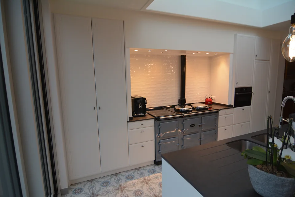 Keuken met witte kastdeuren, fornuis en verlichte tegelwand